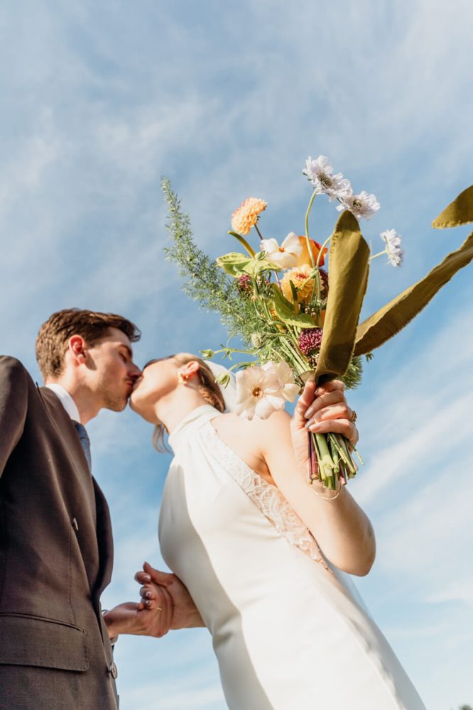 Couple kissing behind a bouquet against a blue sky