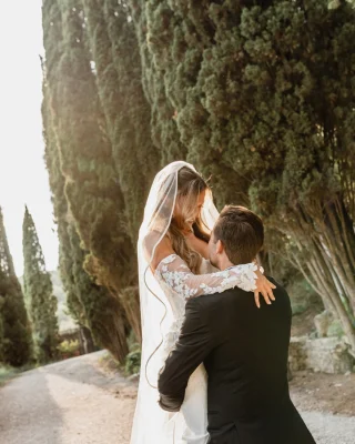 Instagram post: bride and groom embracing beside tall cypress trees