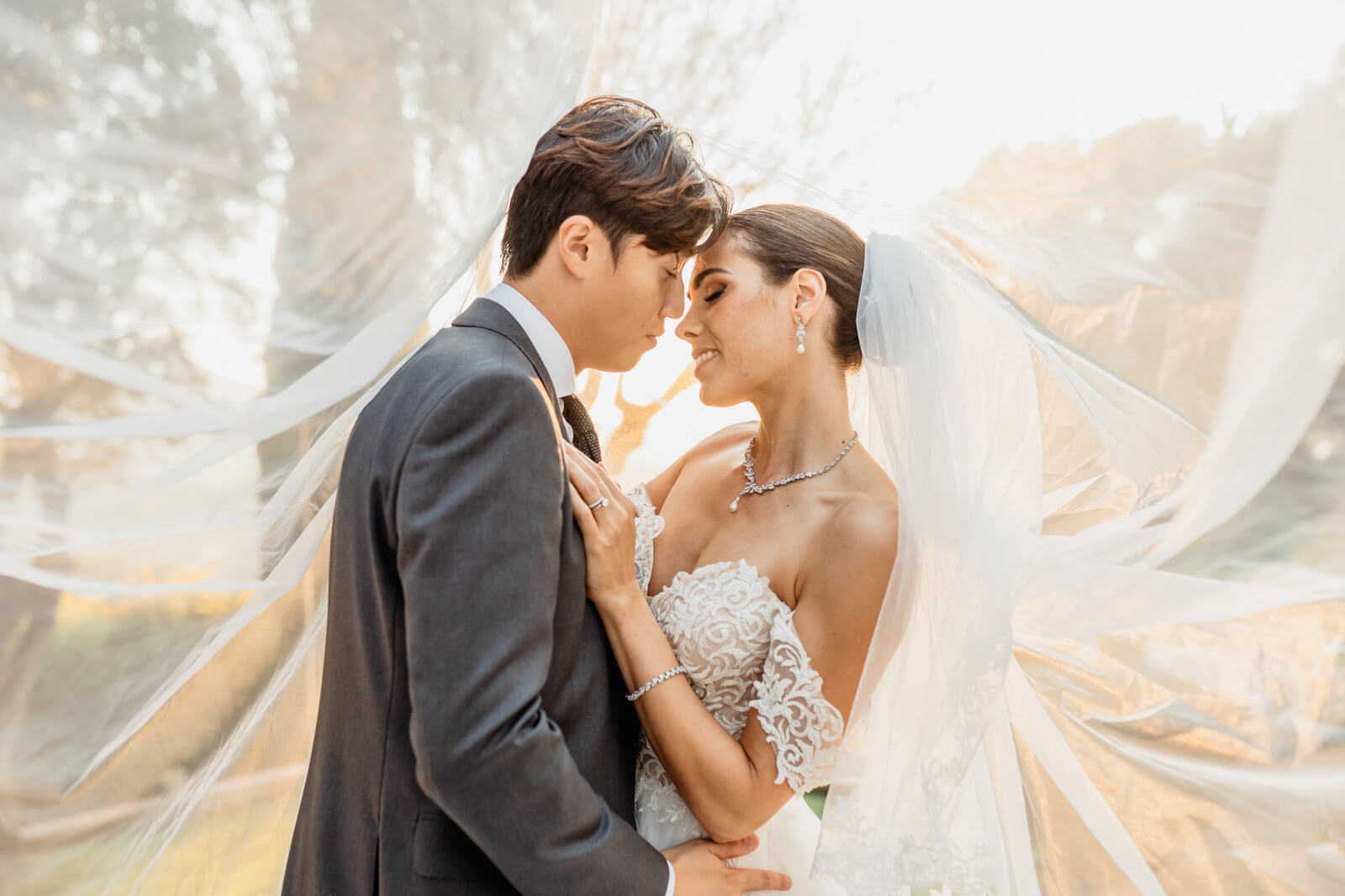 Bride and groom forehead to forehead beneath a flowing veil at golden hour, Barcelona